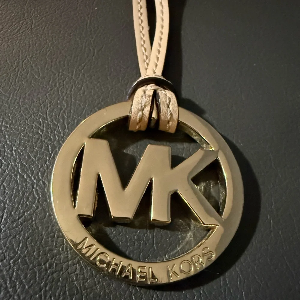 Michael Kors Gold Tone MK Logo Charm With A Light Tan/Creme Color Leather Tassel